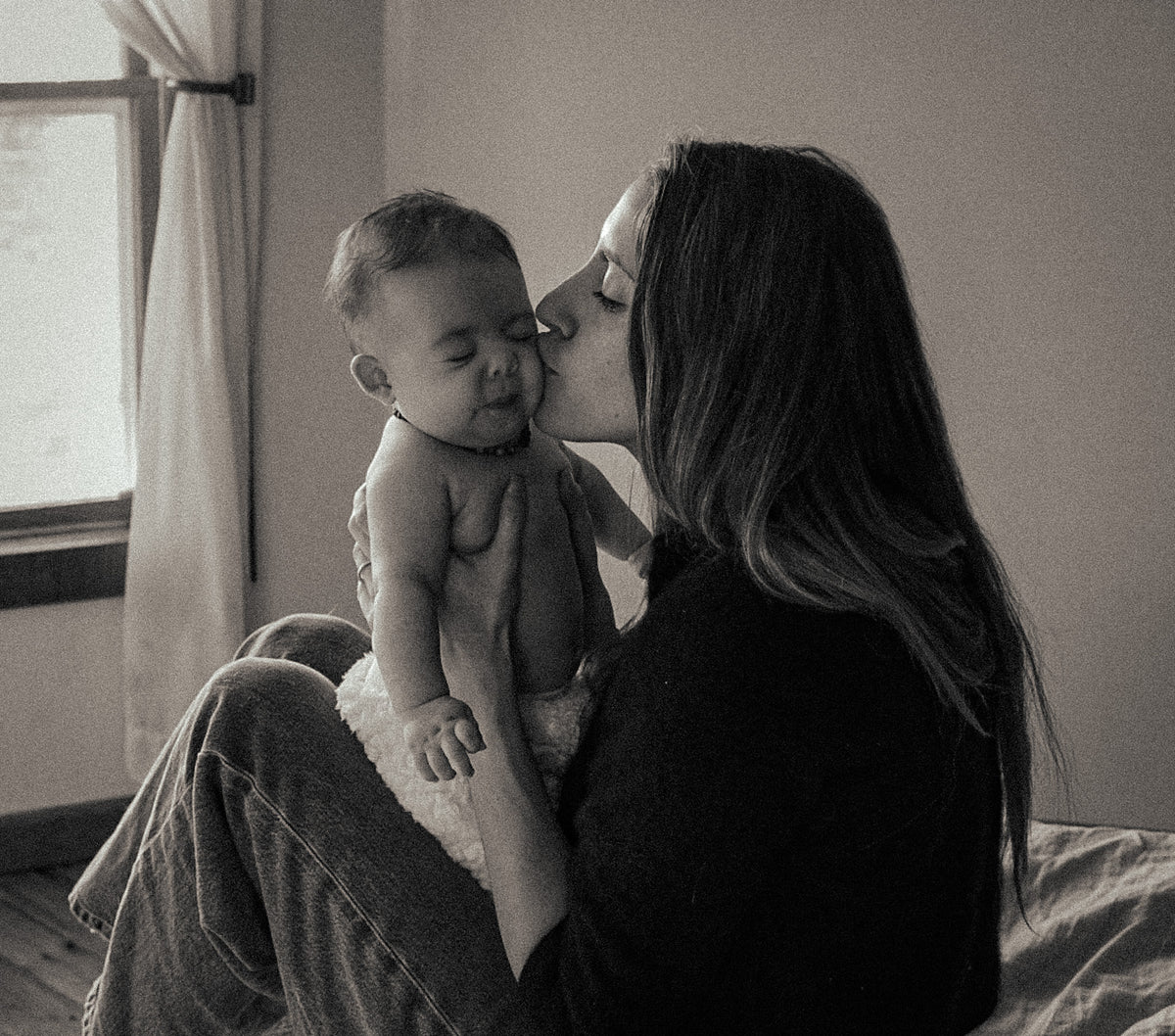 Black and white photo of a woman kissing a baby on the head.